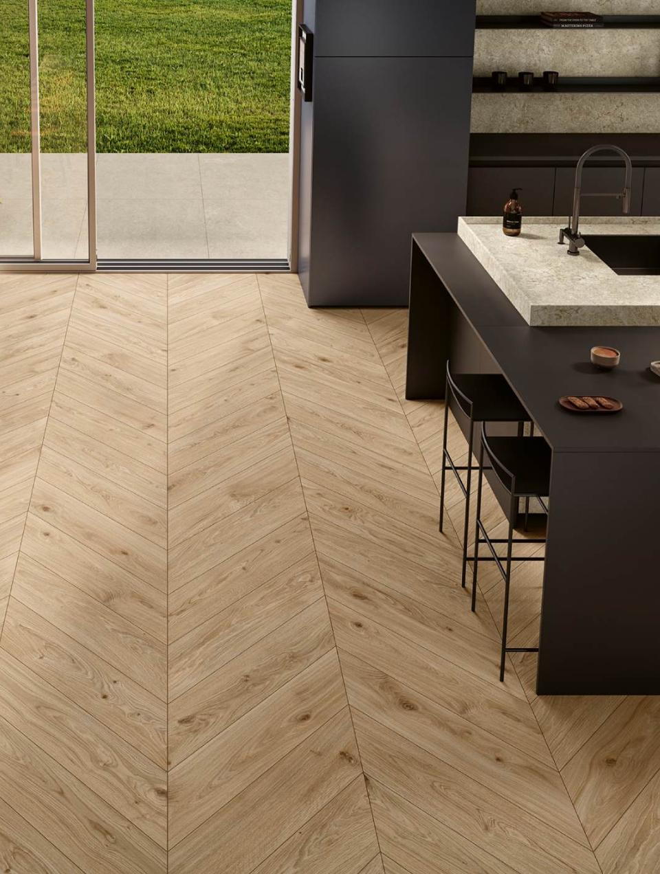 Dark gray lacquered kitchen with a stone island and a gray lacquered dining area, featuring wood-look ceramic tile flooring laid in a chevron pattern