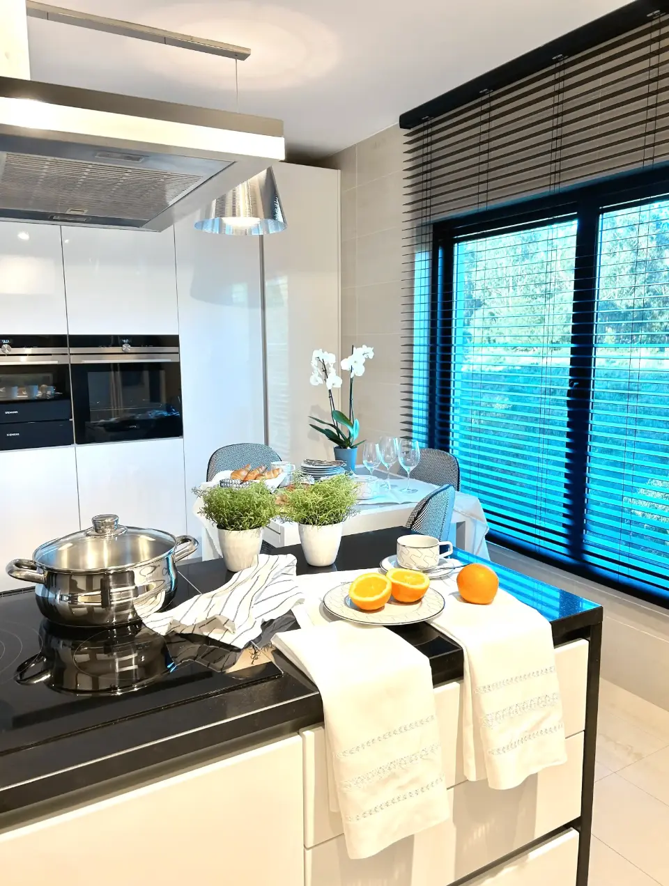 A contemporary white kitchen with clean lines, black countertops, and a dining area featuring a white table and black-and-white chairs