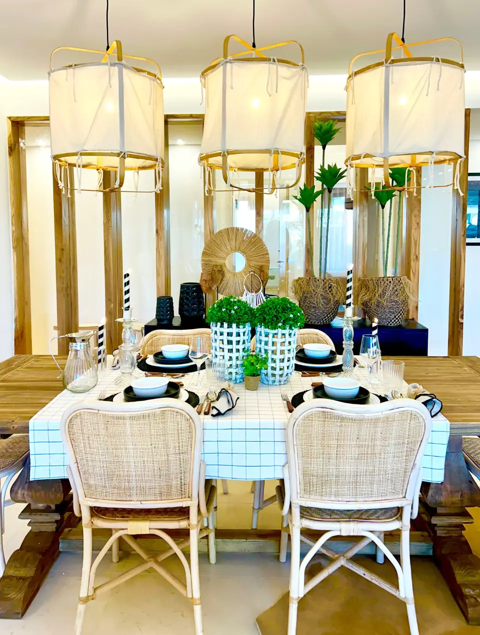 Mesa em madeira, cadeiras em bambu e palha, abatjours pendentes em tecido, peças decorativas étnicas sobre o aparador ao fundo