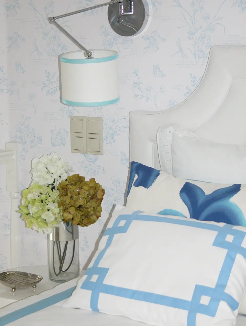 A detail of the bedroom interior design featuring a white cushion with a blue ribbon, romantic wallpaper in shades of blue and white, and a classic he