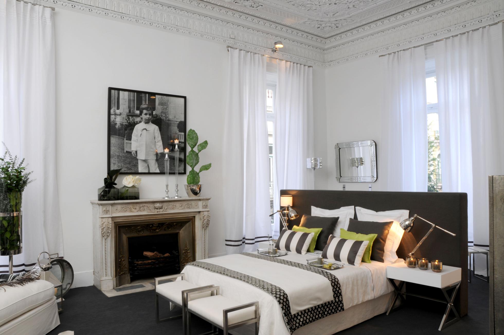 Quarto com tetos ricamente trabalhados decorado com decoração de luxo em tons de branco e cinza, alcatifa cinza no chão e cama confortável