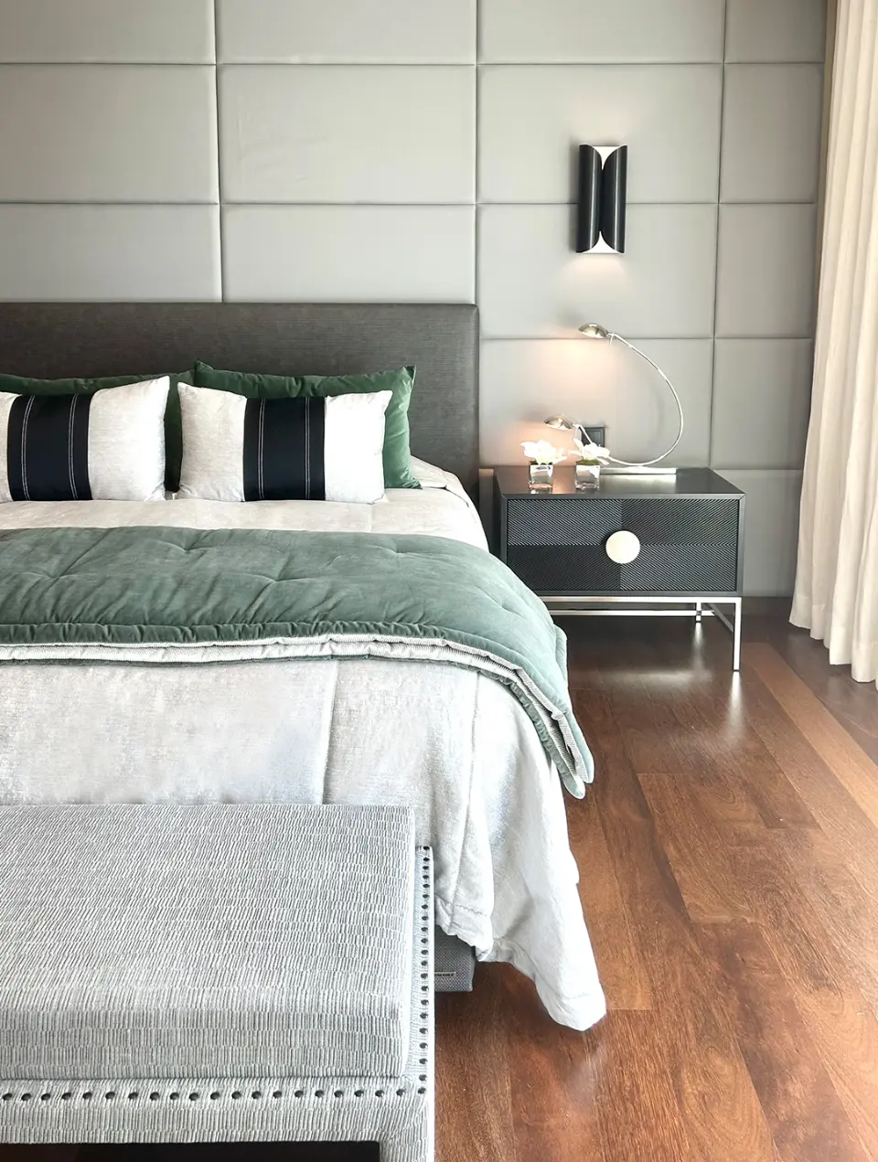 Master suite com estilo contemporâneo, parede da cabeceira apainelada, cama decorada com texteis cinza e apontamentos verde escuro. banqueta estofada 