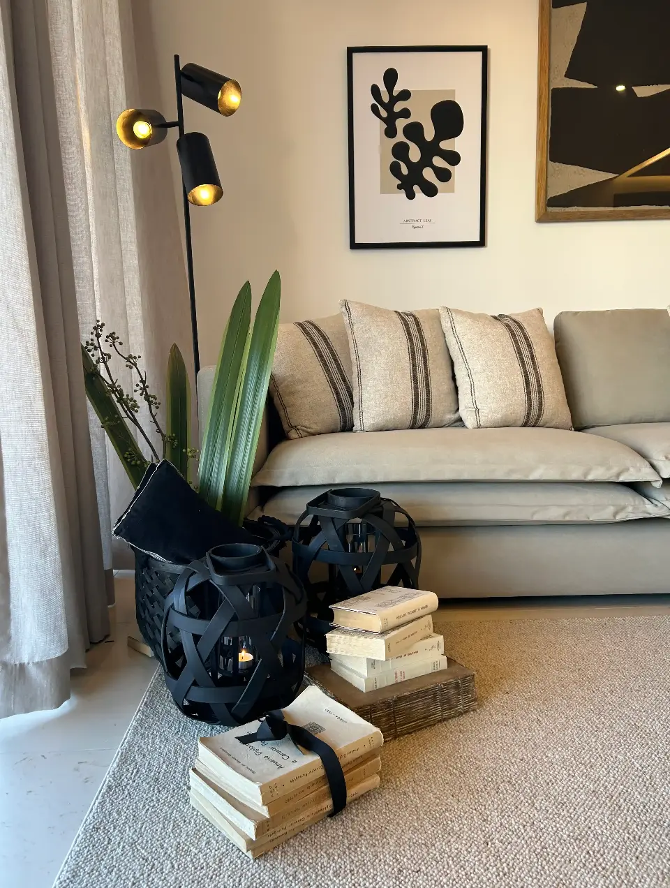 Decorative detail of a living room with a beige sofa, linen cushions, a black floor lamp with two lights and black lanterns.