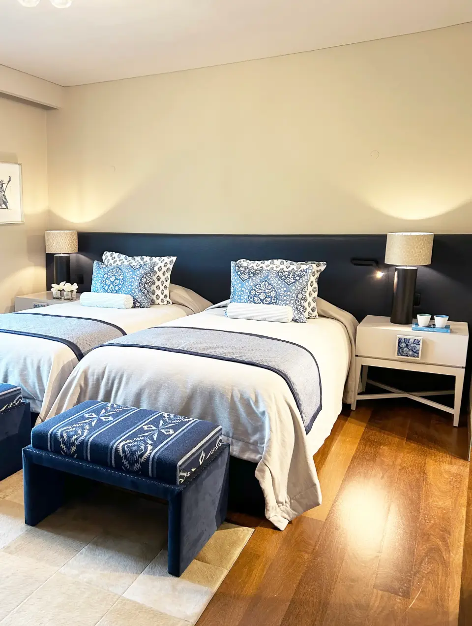 Junior suite decorated in shades of blue and beige, featuring two twin beds, a dark blue head-to-toe headboard, and hardwood flooring
