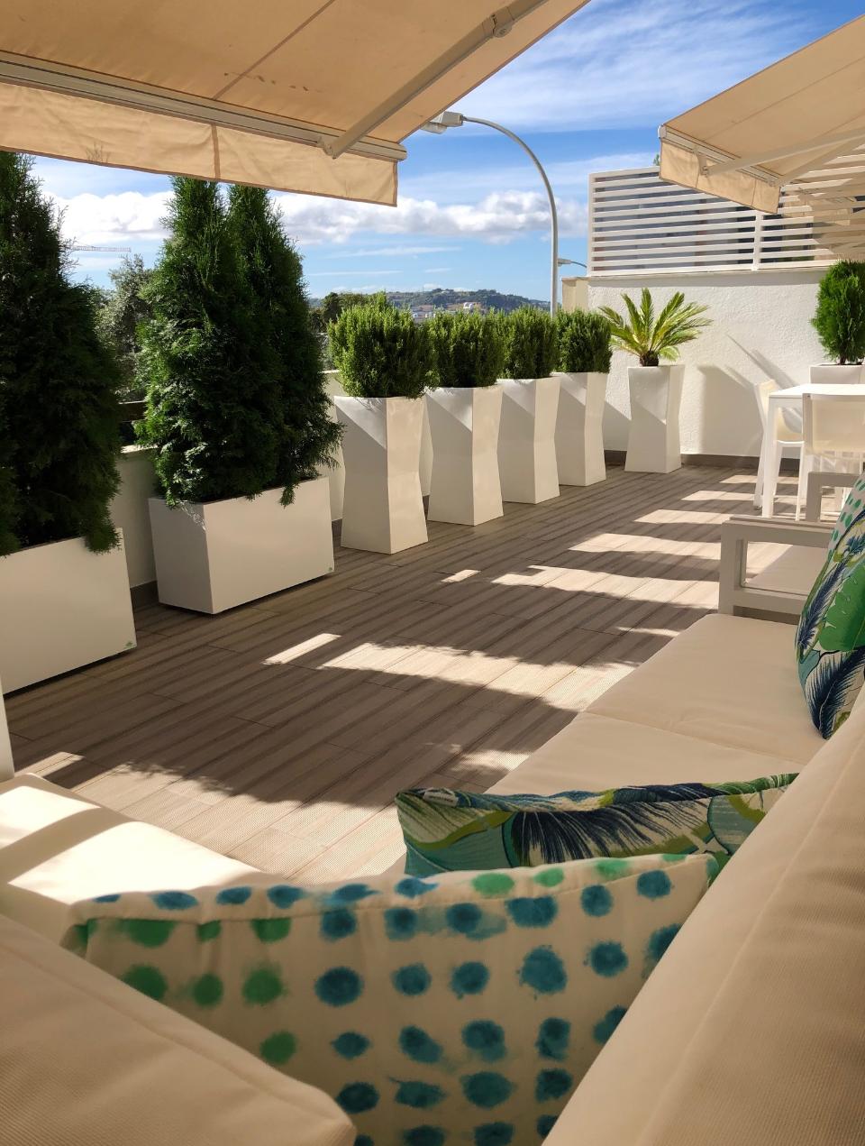 Terraço com zona de estar e refeições. Zona de estar com mobiliário branco e almofadas com padrões em tons de azul e verde