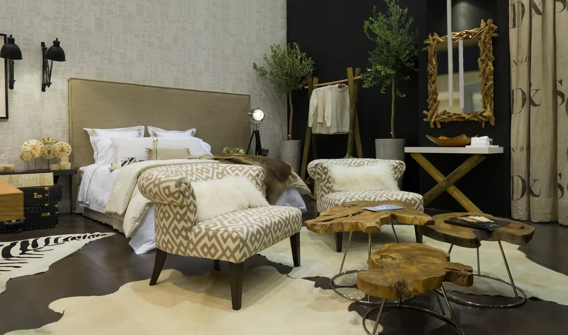 Quarto decorado com tons terra, cabeceira de cama assimétrica, cadeirões estofados com tecido de padrão étnico e  tapetes de pele de vaca