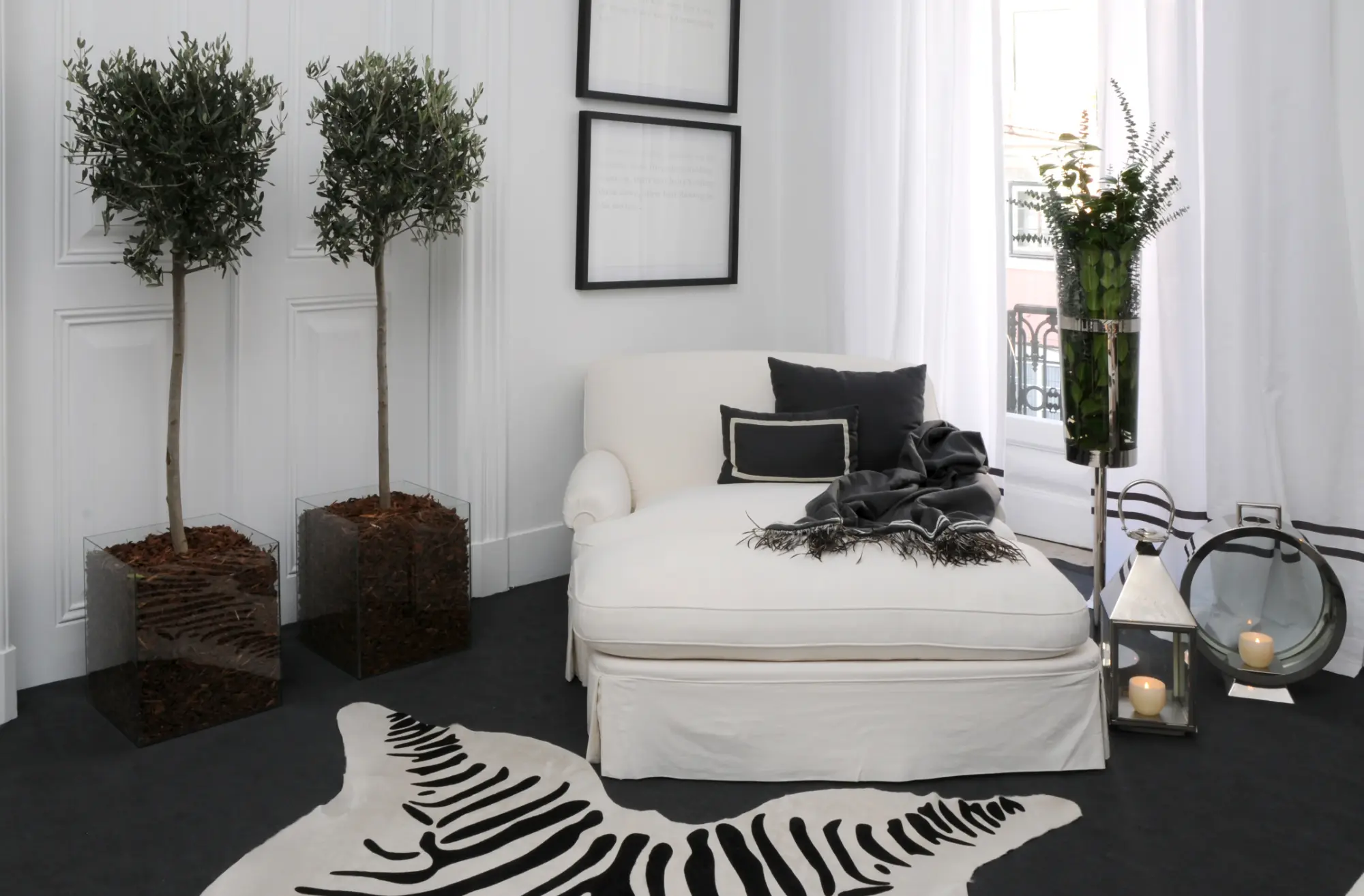 Detalhe de decoração de suite com cadeirão com banqueta muito confortável branco, tapete efeito zebra e oliveiras naturais