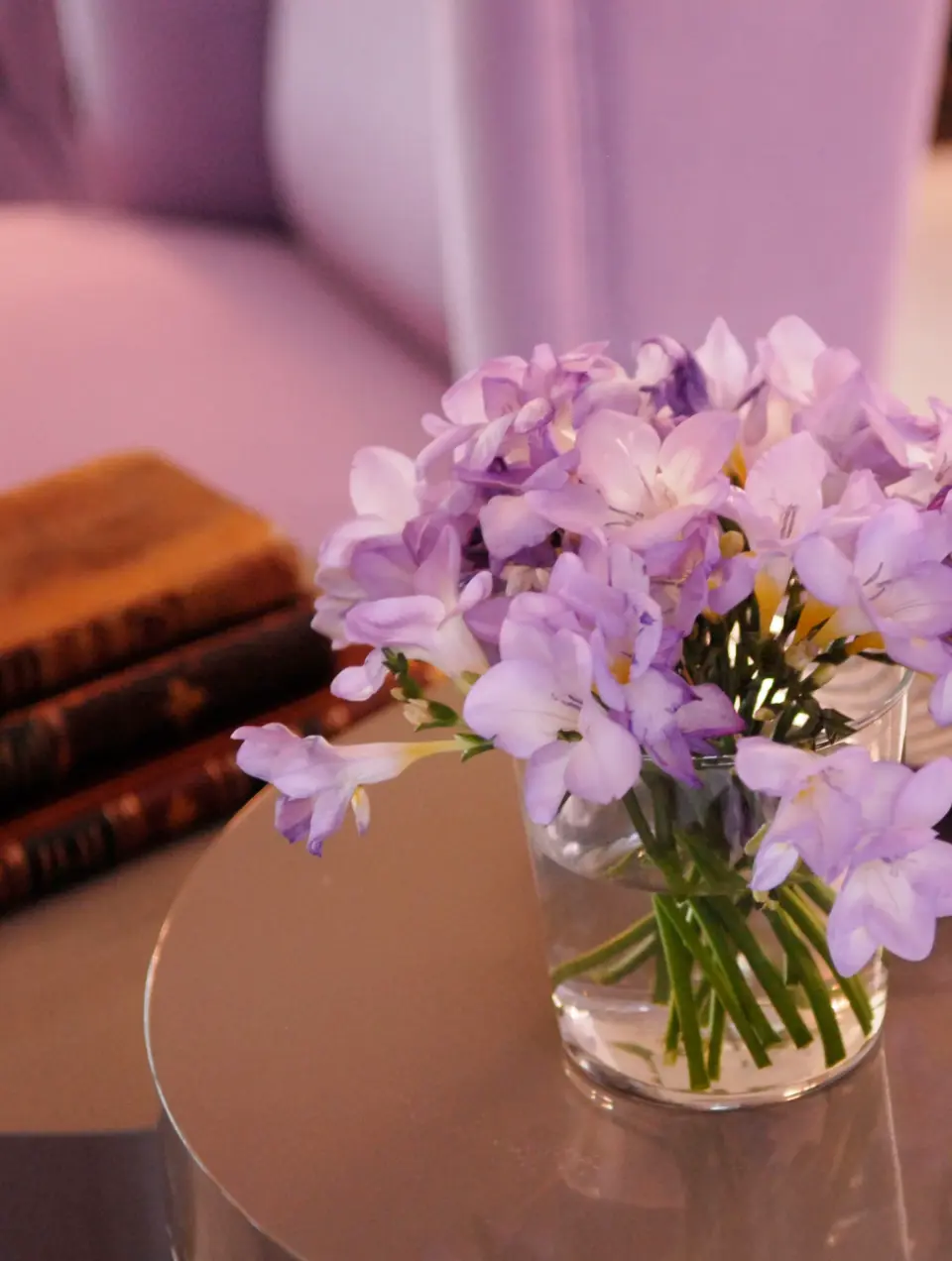 Detalhe de decoração de vaso de vidro com flores lilases sobre mesa de apoio lacada a taupe 