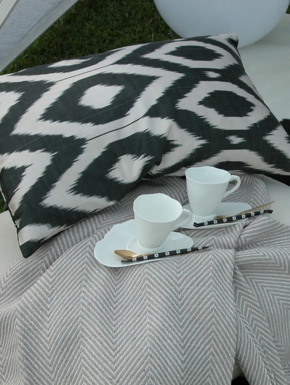Detalhe de uma decoração com manta beige, almofada de seda preta e branca e chávenas de dessign contemporâneo