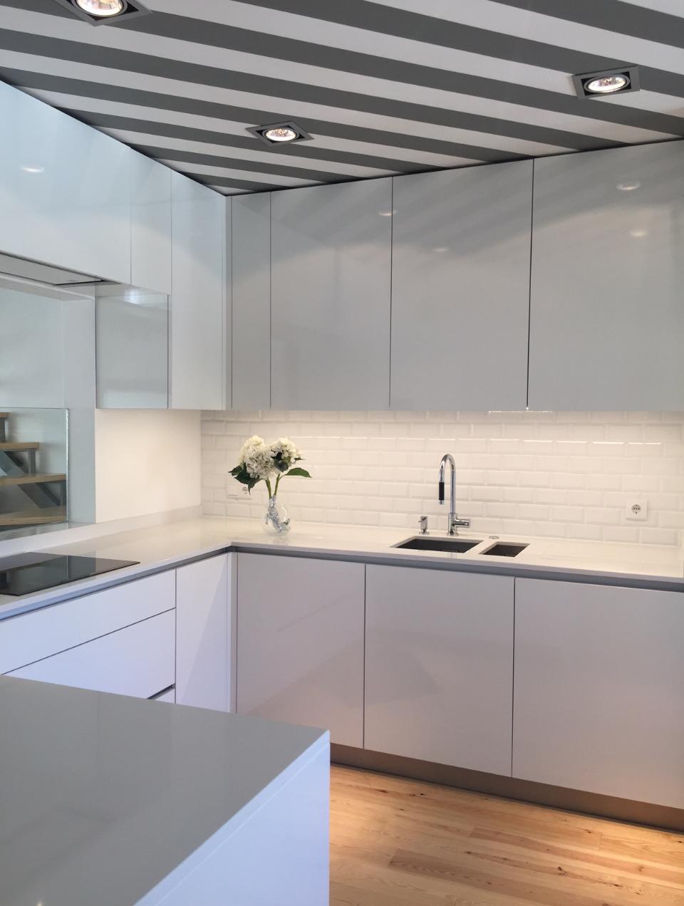 A contemporary-style kitchen opening onto the living room, featuring white lacquered units, wooden flooring and a ceiling with white and grey stripes