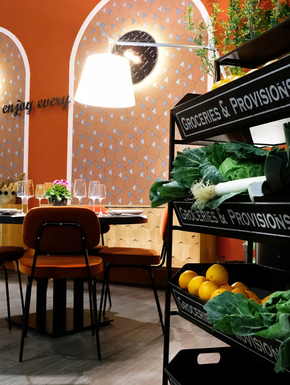  Restaurant with an orange accent wall featuring decorative arches covered in wallpaper, orange upholstered chairs, and an industrial bookshelf displa