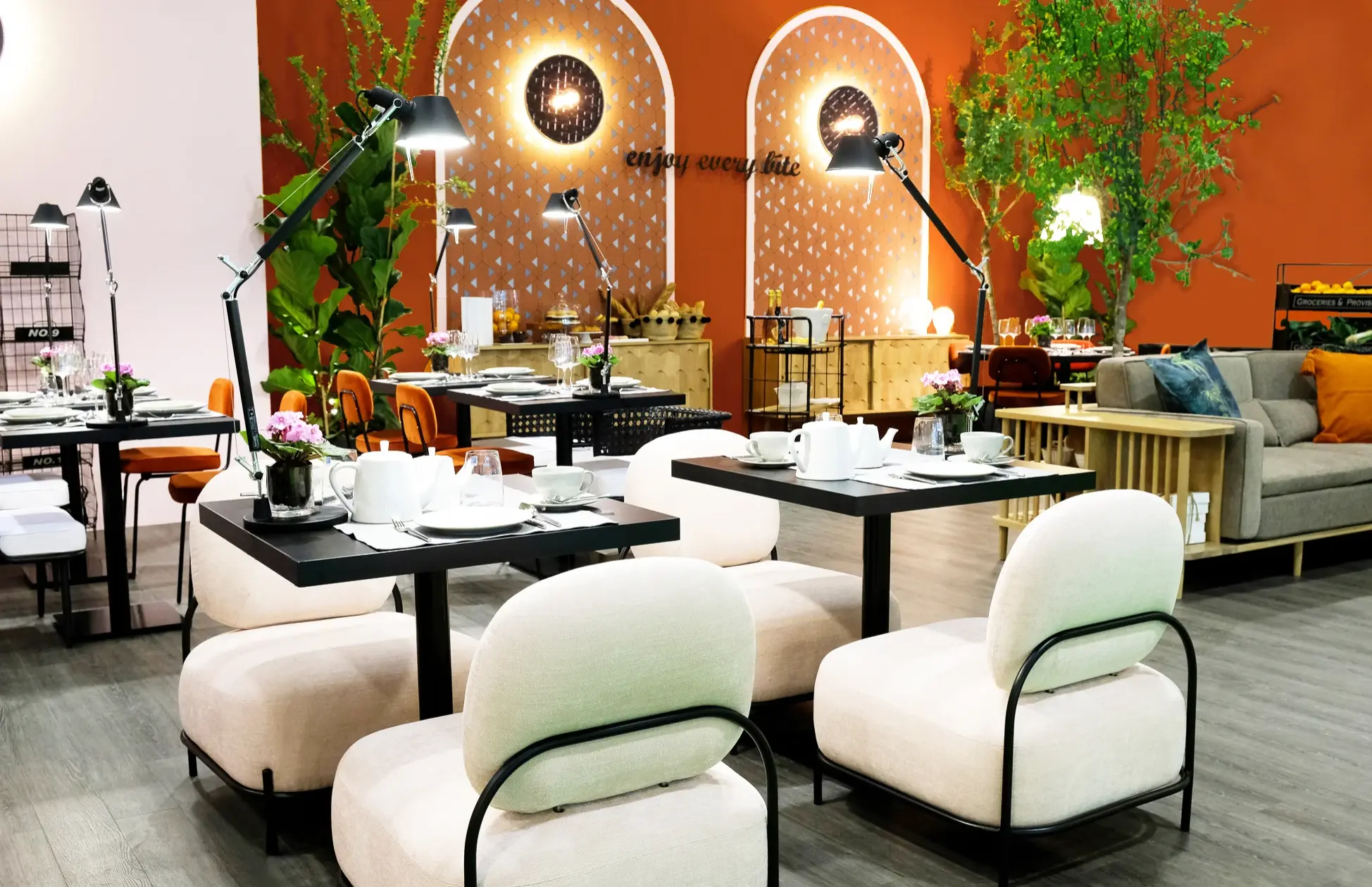 Restaurant with industrial decor, black tables, light pink armchairs, and wicker chairs. Orange back wall featuring arches
