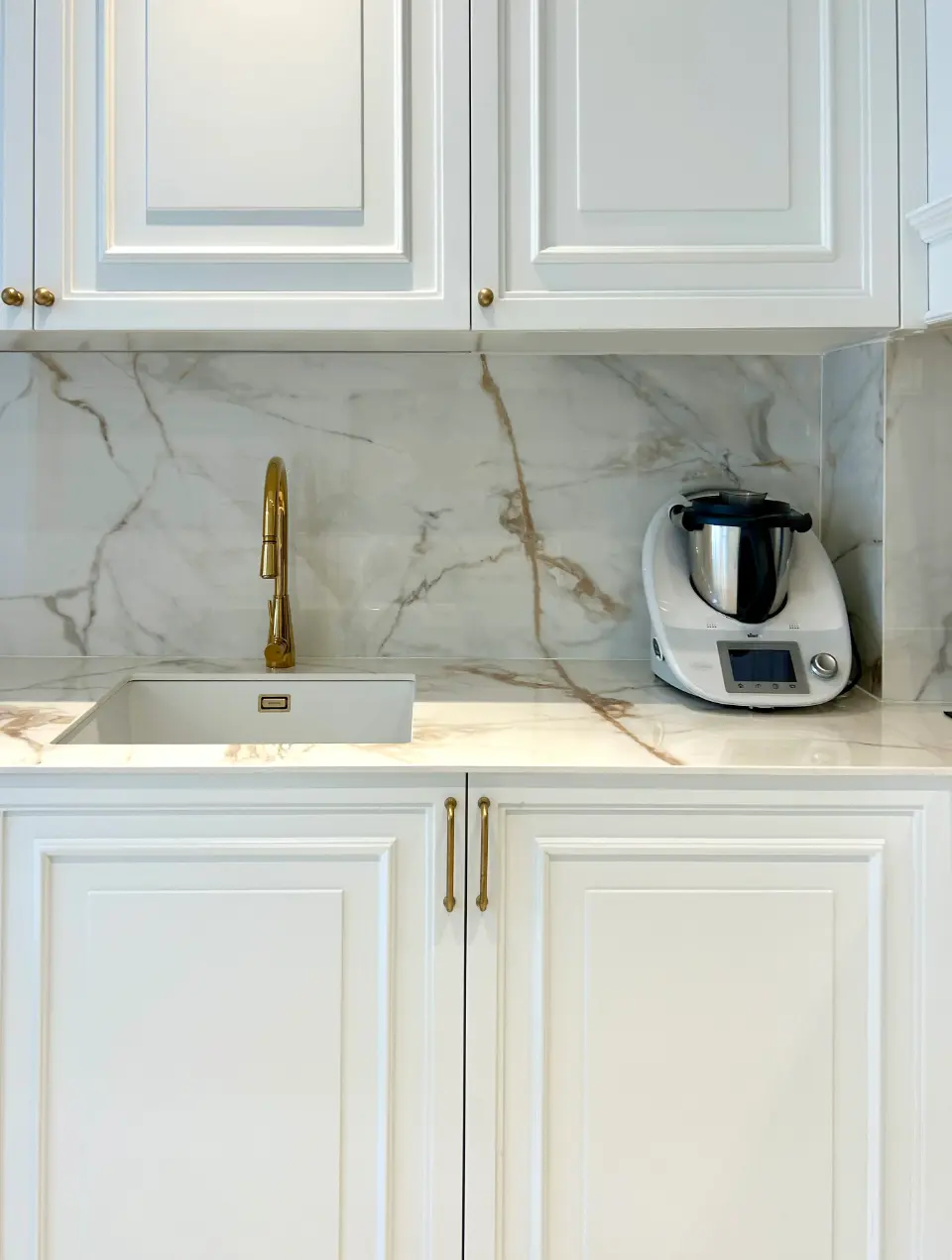 A classic white-lacquered kitchen with paneled doors and gold-colored handles, designed by Margarida Bugarim Interiores