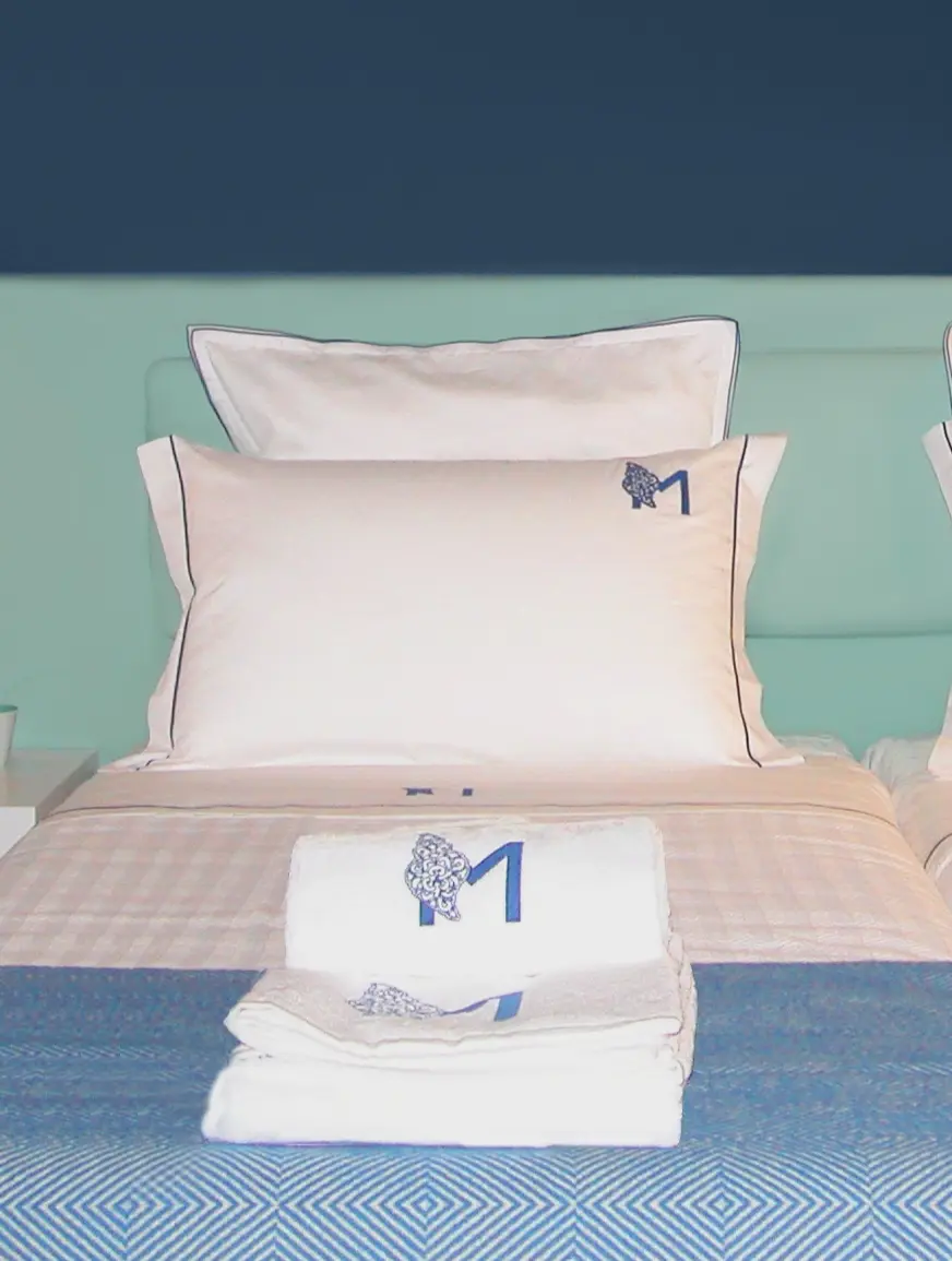 Decoração de quarto de hotel em tons de azul com roupa de cama e atoalhados com logotipo bordado- logotipo desenvolvido por Margarida Bugarim