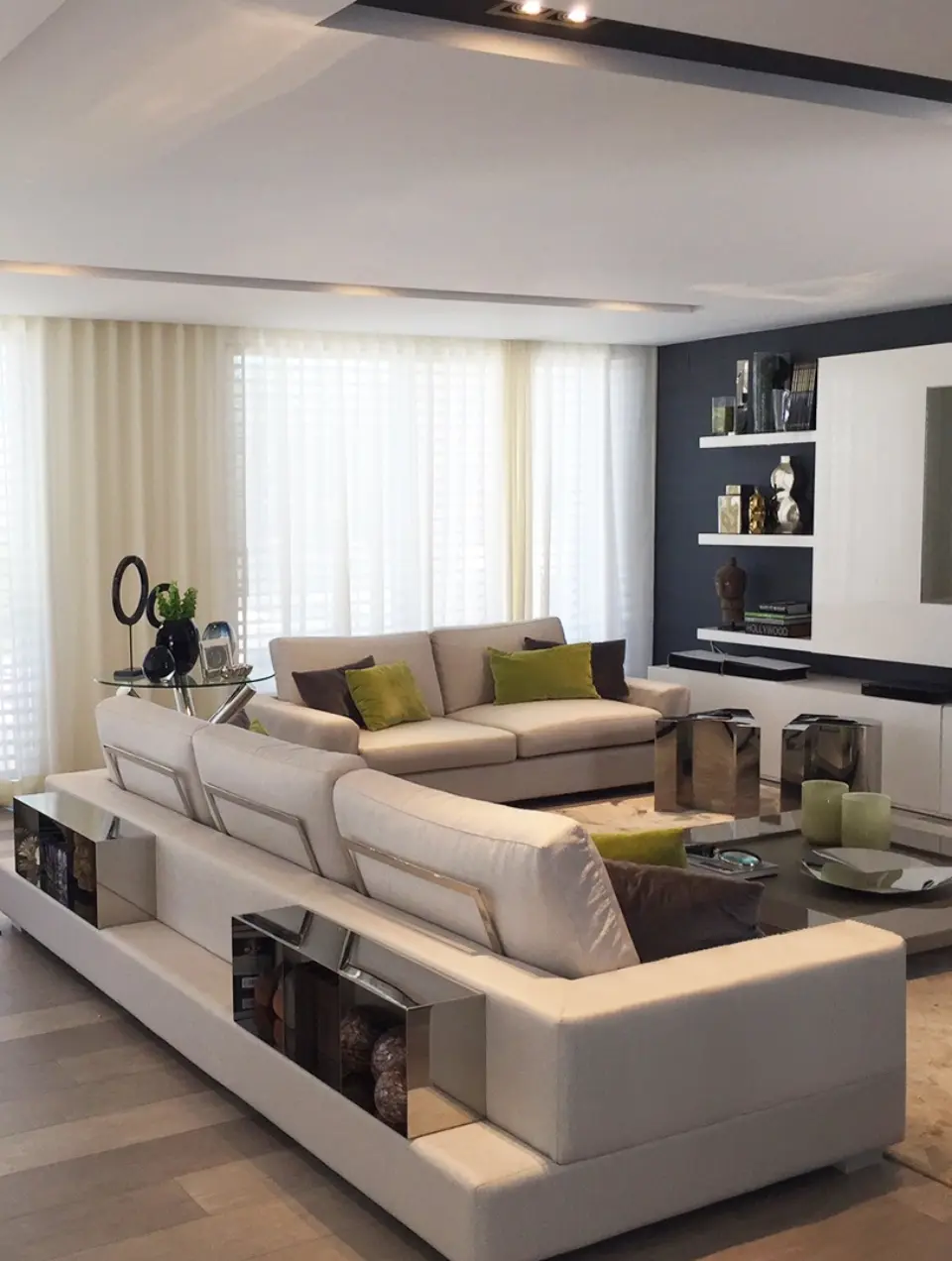 Decoração de zona de TV de sala com dois sofás de linhas contemporâneas estofadas com tecido beige e com detalhe de prateleiras em inox