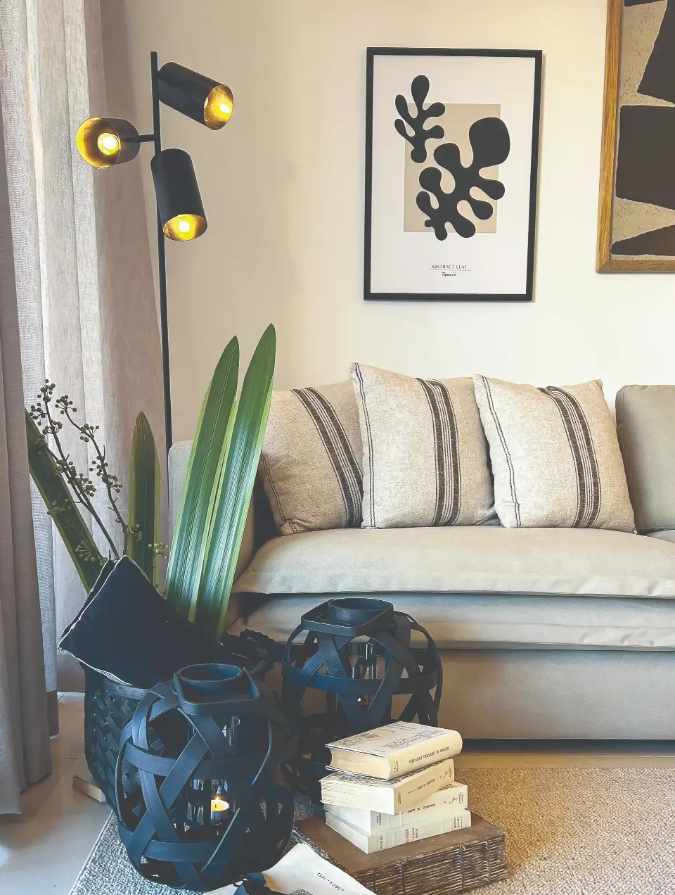 Detalhe de decoração de sala com sofá de capas em algodão beige, lanternas pretas e candeeiro de pé preto.