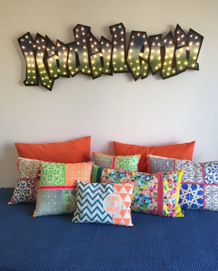 Quarto jovem com painel personalizado com nome em graffity e almofadas muito coloridas.