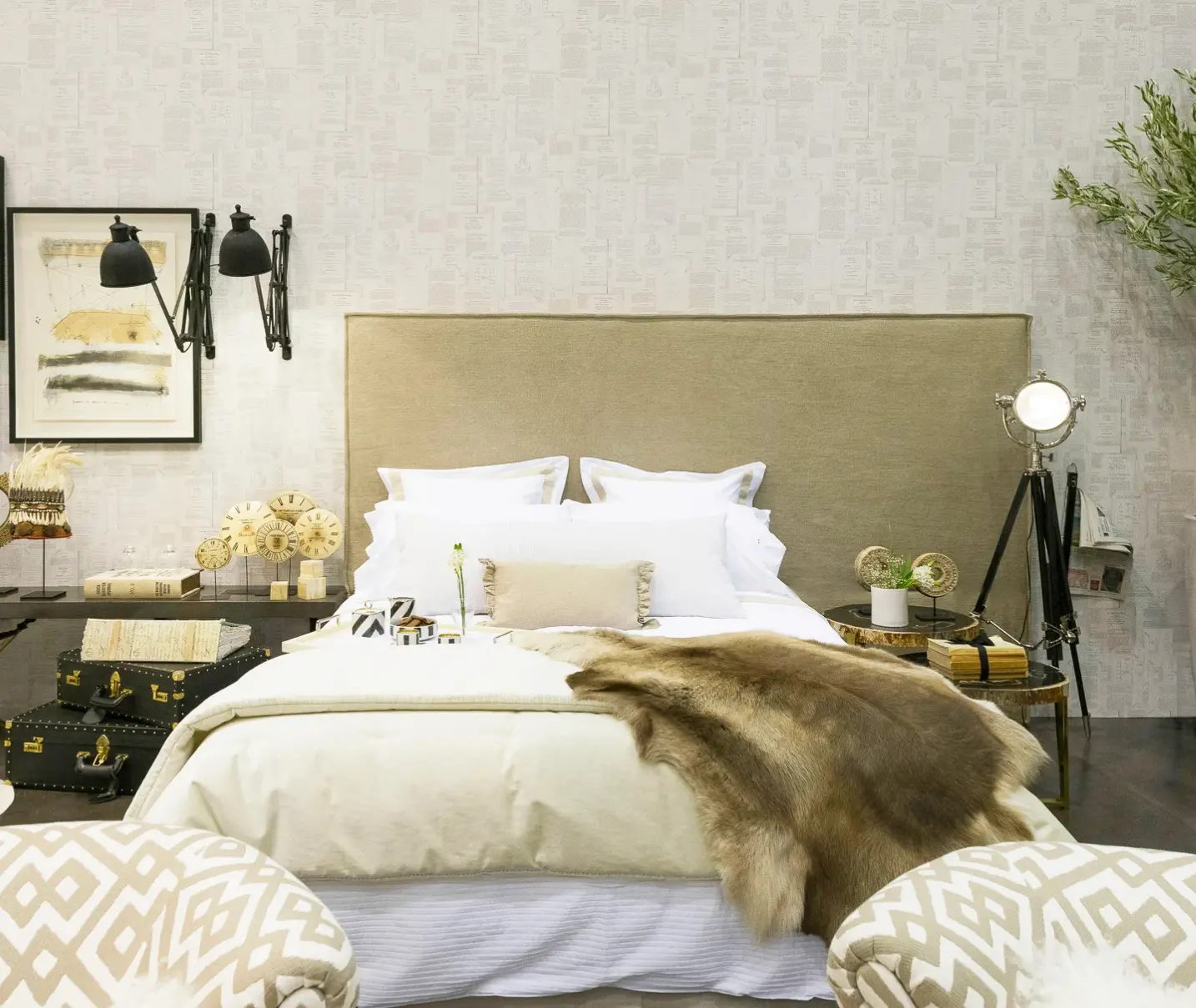 Bed with asymmetrical headboard upholstered in beige linen, very comfortable white bedding and fur blanket, industrial wall lamps, and wallpaper