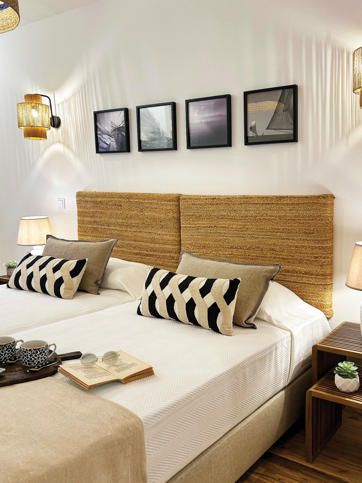 Quarto com duas camas, cabeceiras de cama em corda natural, almofadas decorativas de padrão, apliques em ratan e quadros de motivos náuticos