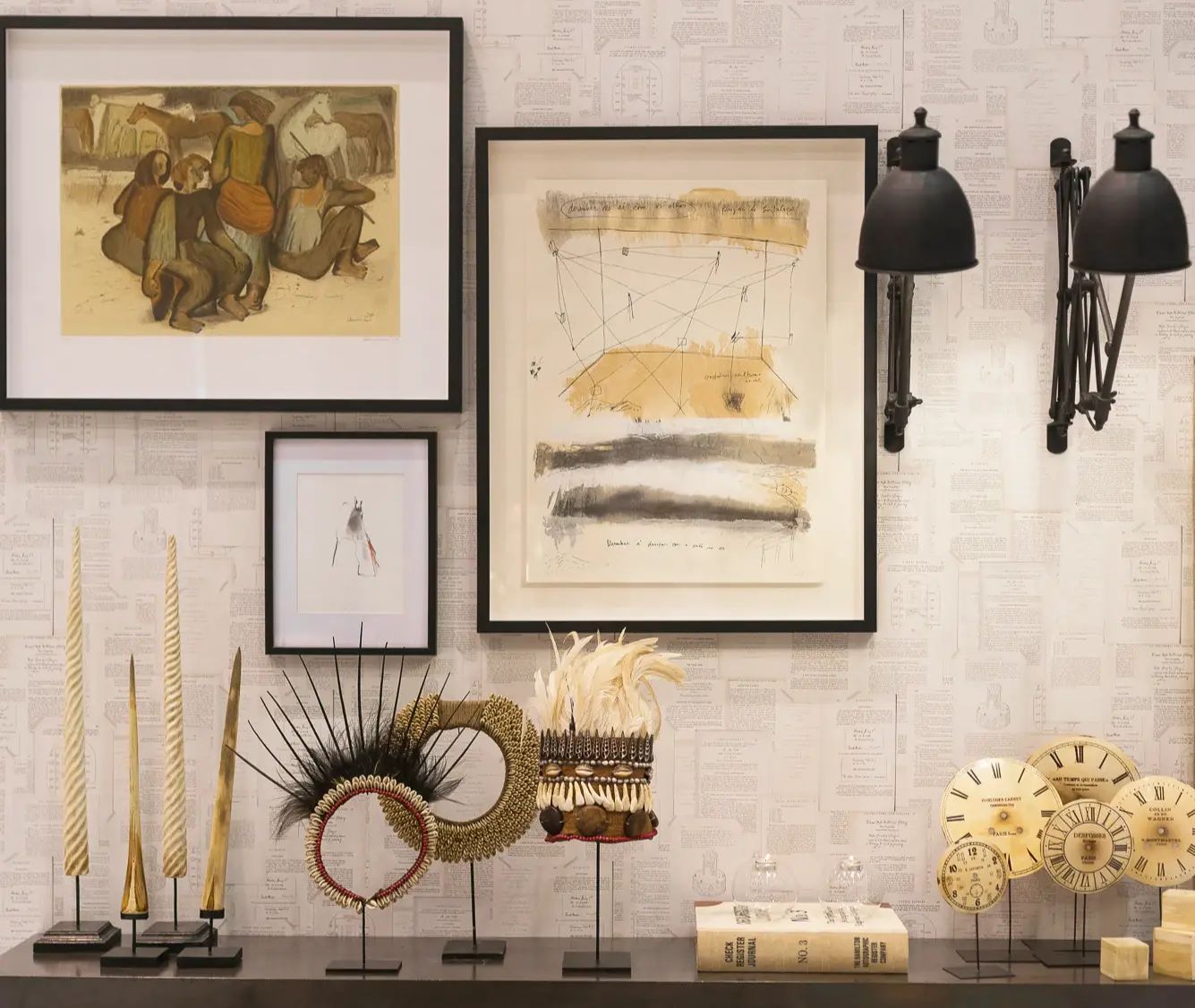 Wall lined with paper featuring book pages with two industrial wall lamps and frames, shelf with crowns and ethnic necklaces