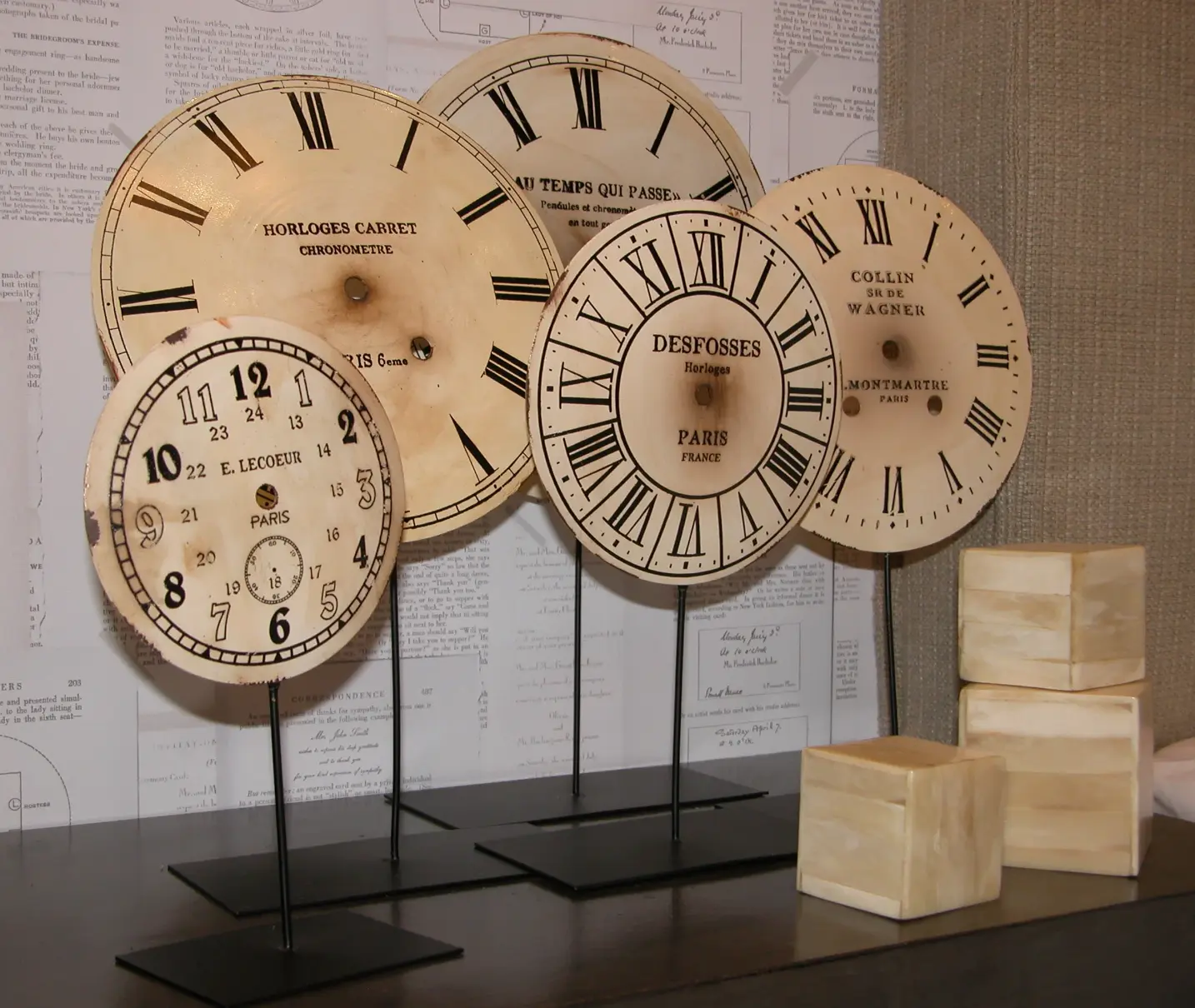 Detail of antique clocks on a shelf with wallpaper featuring book page prints in the background