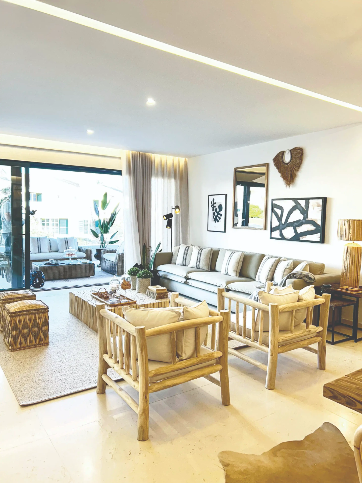 Sala decorada em tons de beige com cadeirões de madeira tosca, mesa de troncos, puffs em palhinha, e sofá beige
