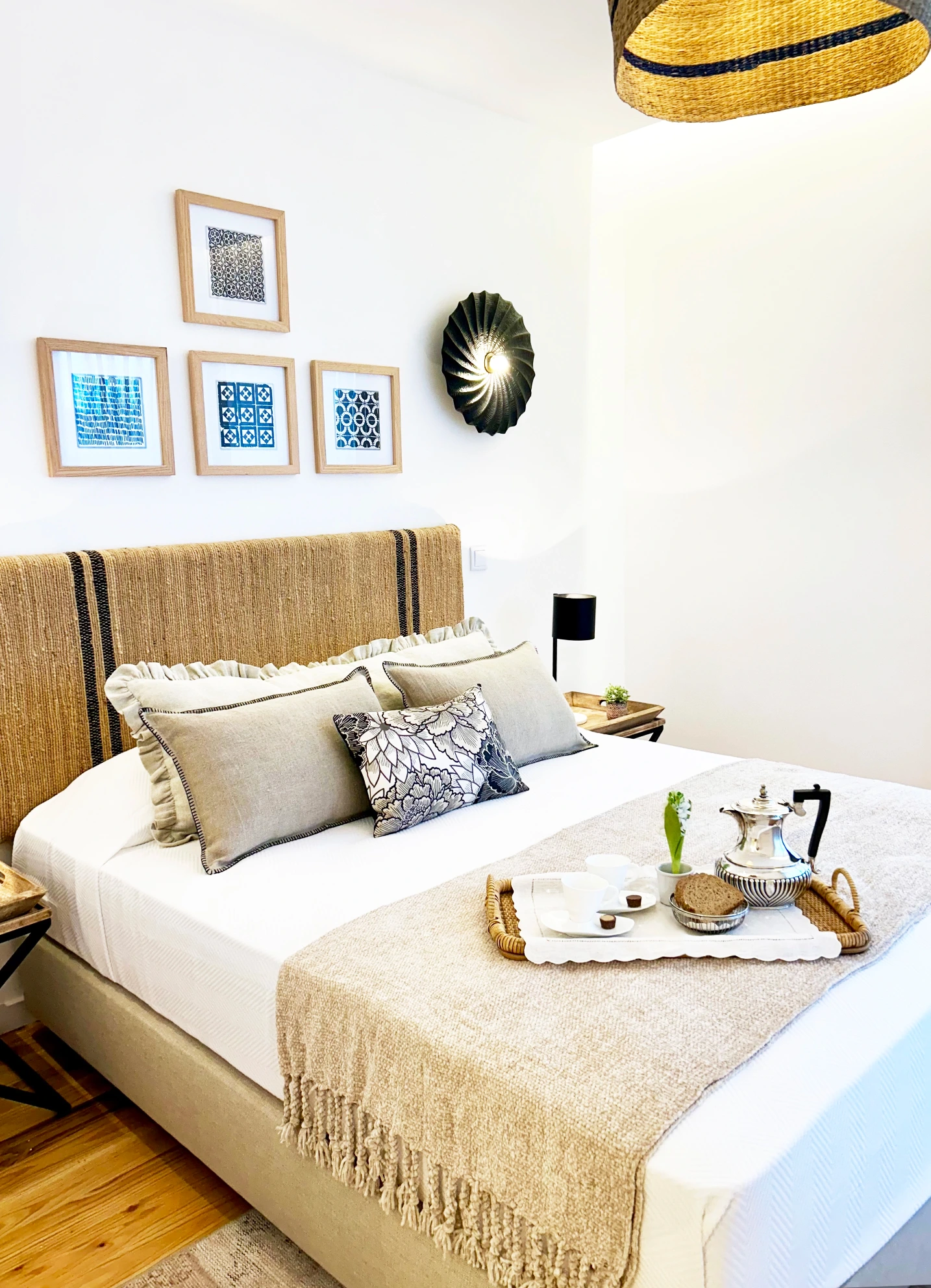 Decoração de suite em tons neutros, cabeceira de cama  de textura natural com riscas pretas às pontas, apliques pretos e quadros com padrões em preto e branco