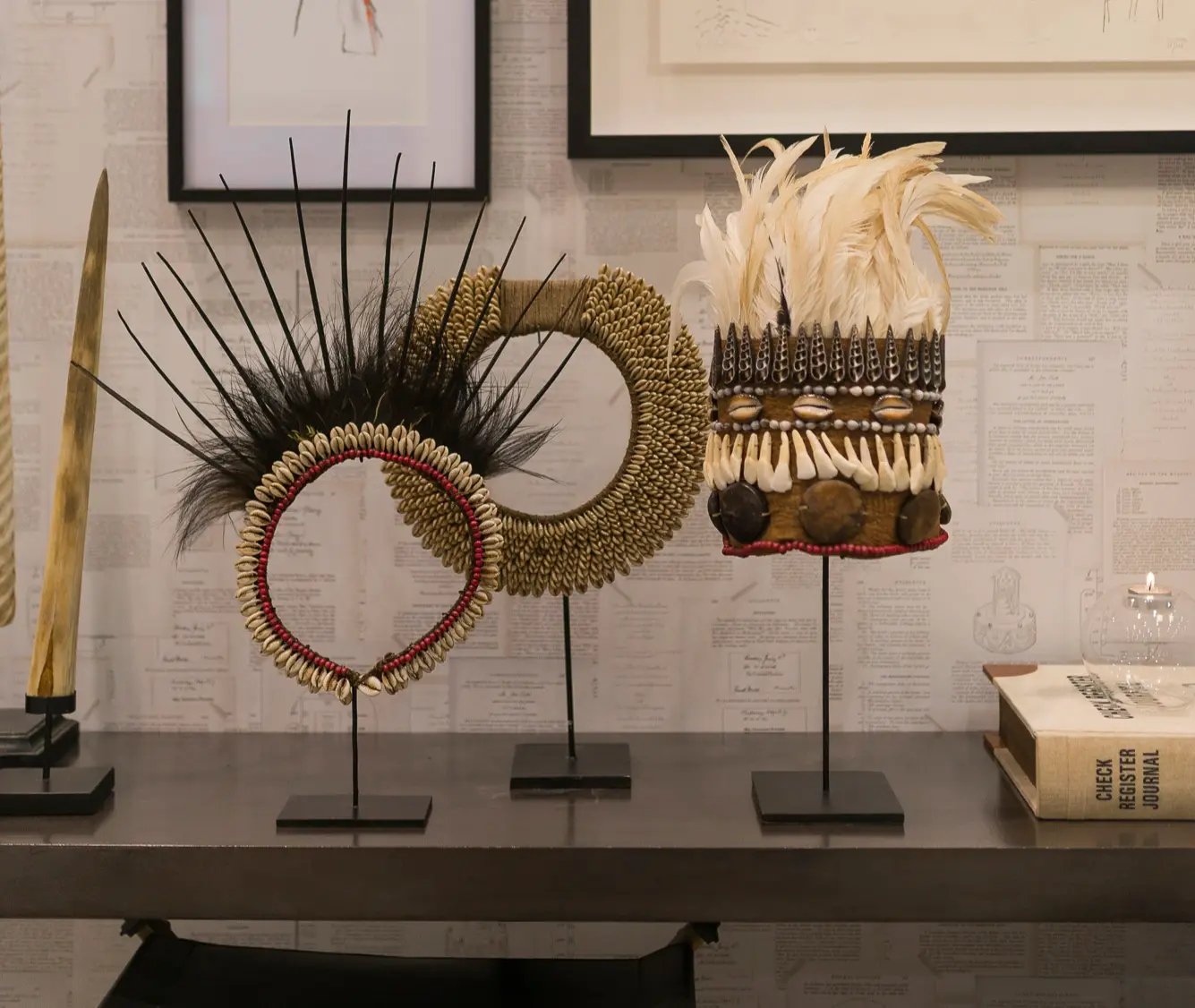 Tribal crowns and necklace on a microcement shelf. Back wall lined with paper featuring book pages. 