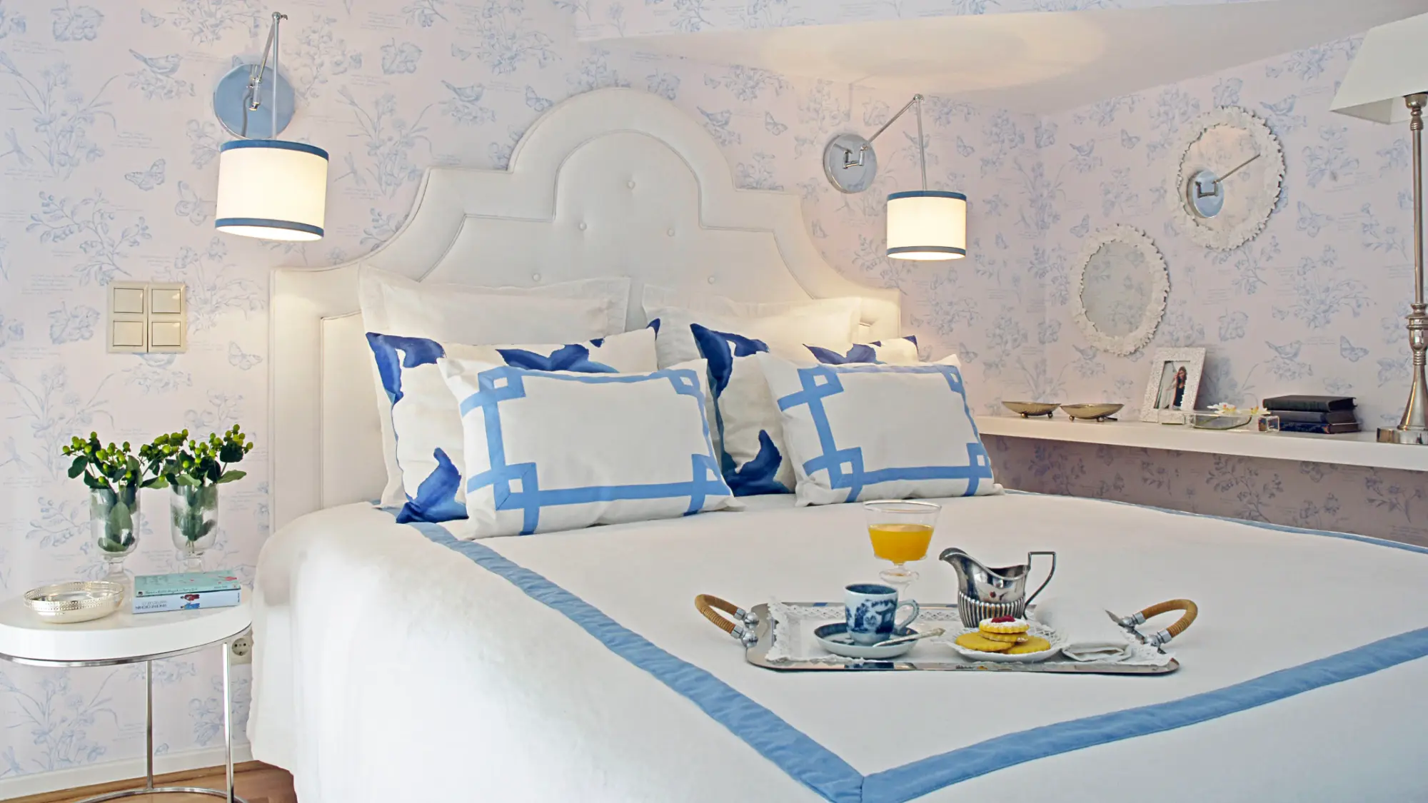 Quarto clássico e muito feminino com aplicação de papel de parede floral, tecidos confortáveis brancos e apontamentos decorativos azuis.