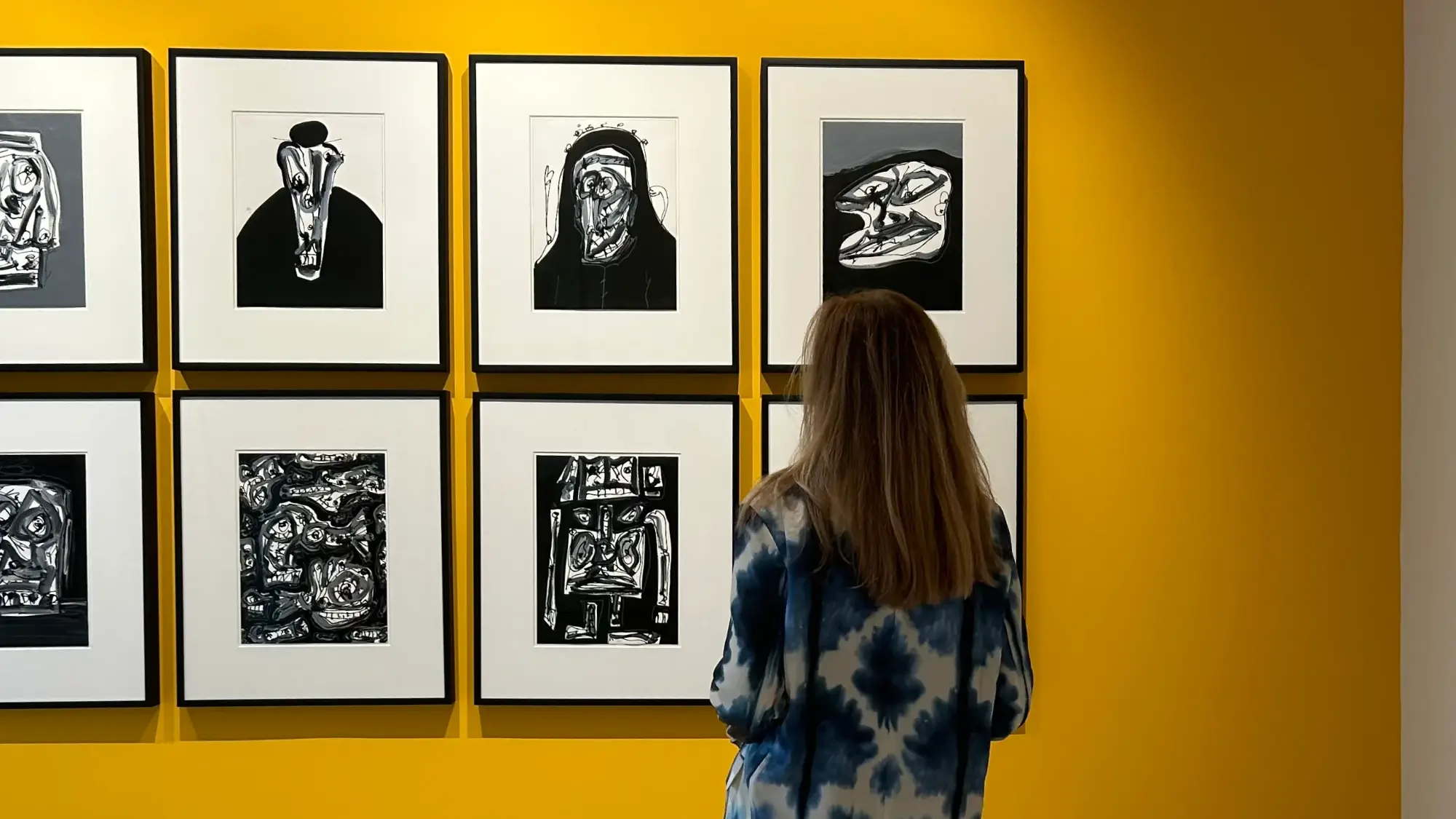 Designer de interiores Margarida Bugarim em exposição de arte contemporânea com obras em preto e branco numa parede de destaque pintada de amarelo