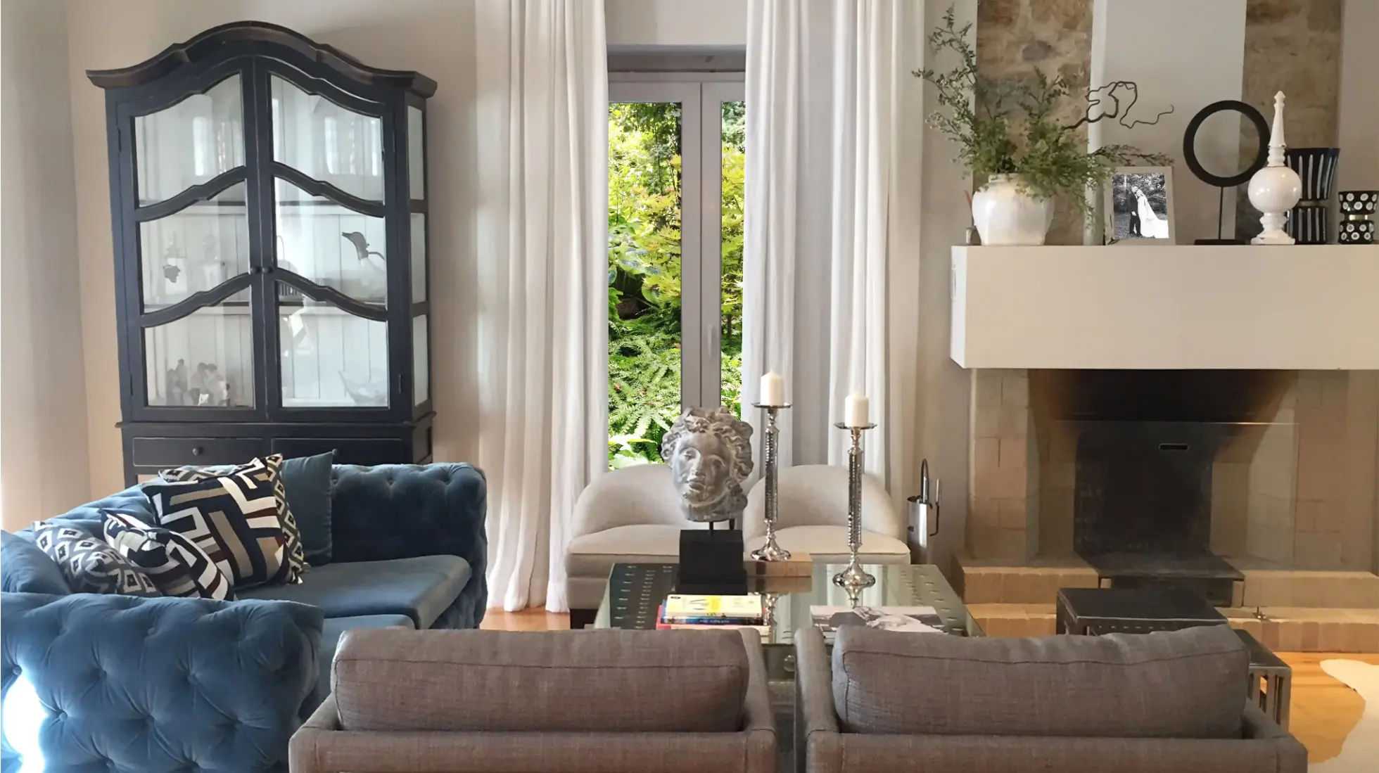 Sala de estar com lareira, sofá clássico em veludo azul, cadeirões contemporâneos cinza, mesa de centro em espelho com peças decorativas